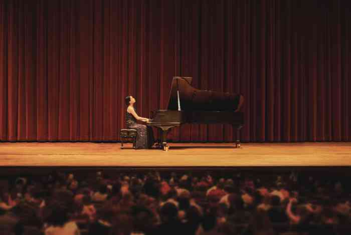 a woman playing piano in a concert in front of a large crowd