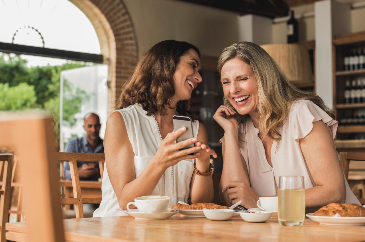 two women chatting together in a restaurant and looking at a mobile phone