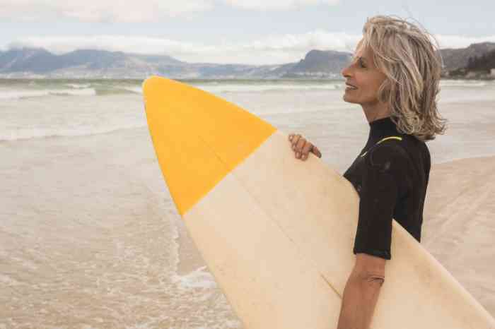 a senior woman holding a surfboard on the beach