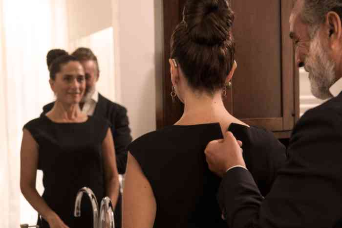 man zipping up a woman's dress as she watches in the mirror
