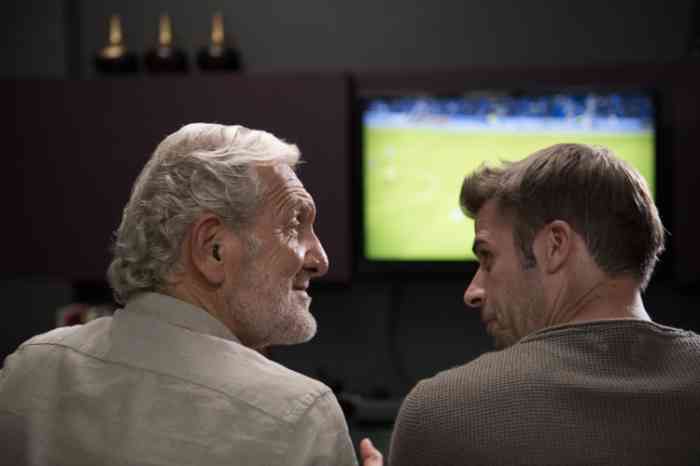 grandfather and grandson watching a football match on tv on their sofa