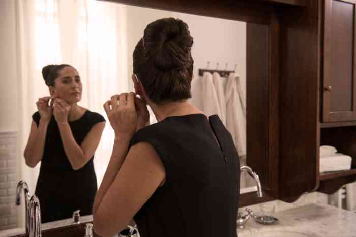 A girl looking at herself in the mirror while putting on an earring