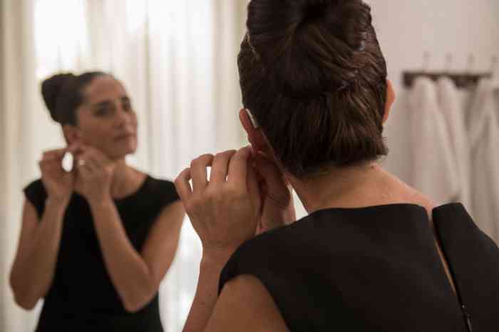 a woman arranging her hearing aid looking herself at the mirror