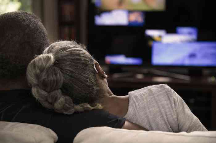 a woman wearing a hearing aid and watching tv with her husband in the living room