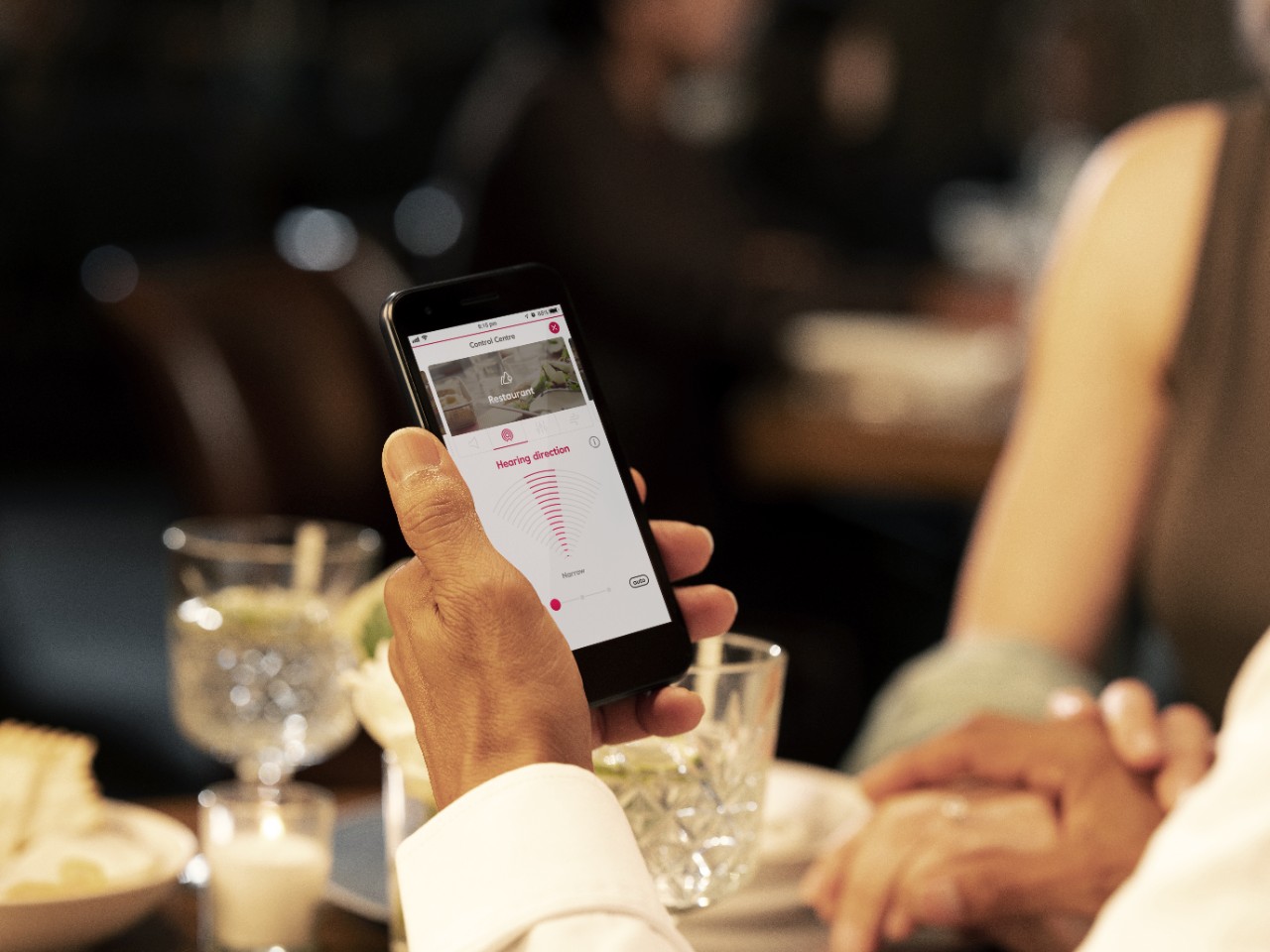 A man holding a phone reading an Amplifon article during dinner
