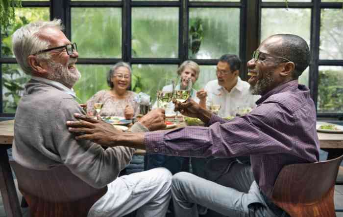 elderly men and women laughing together with glasses of white wine
