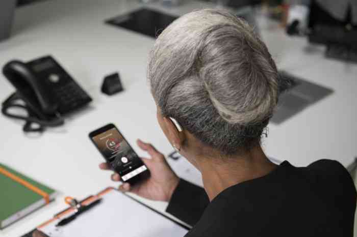 Old woman checking her phone wearing an Amplifon hearing aid