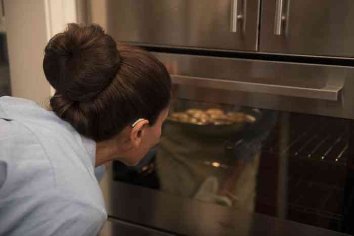 woman wearing a behind the ear hearing aid looking at something cooking in the oven