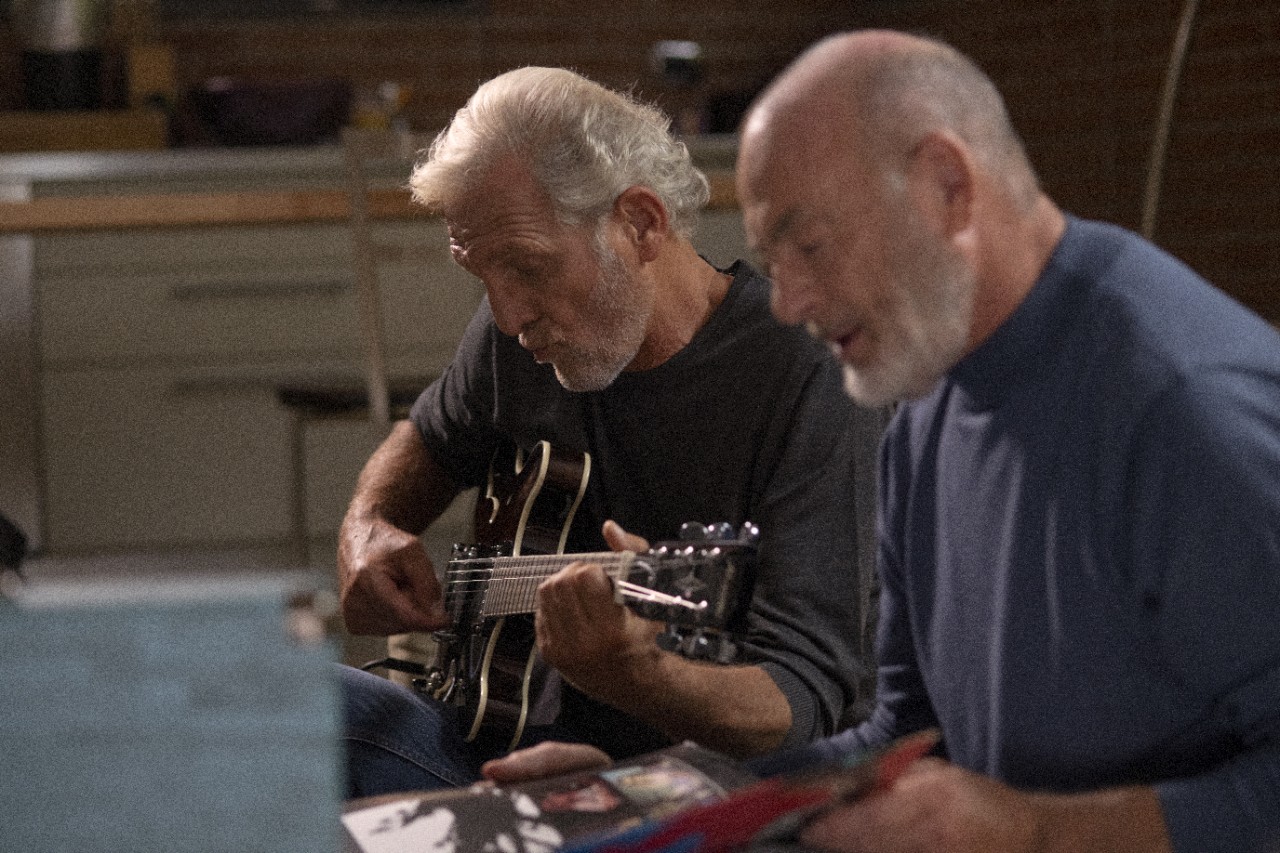 two elderly men playing guitar on a sofa