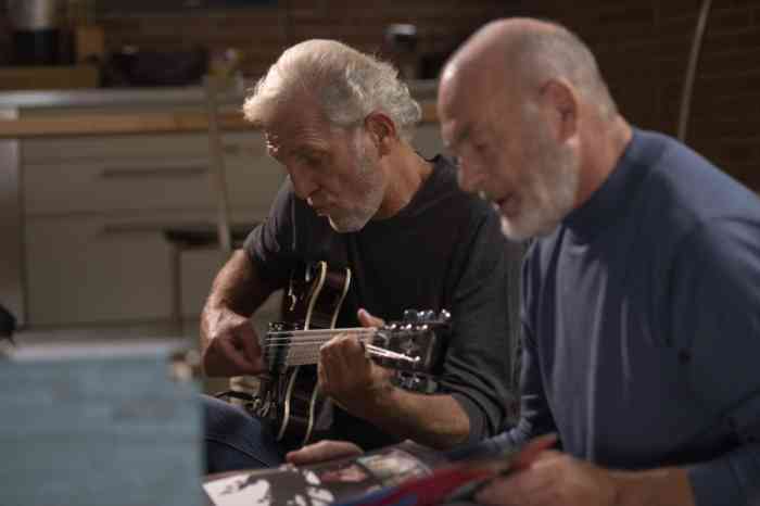 two elderly men playing guitar on a sofa