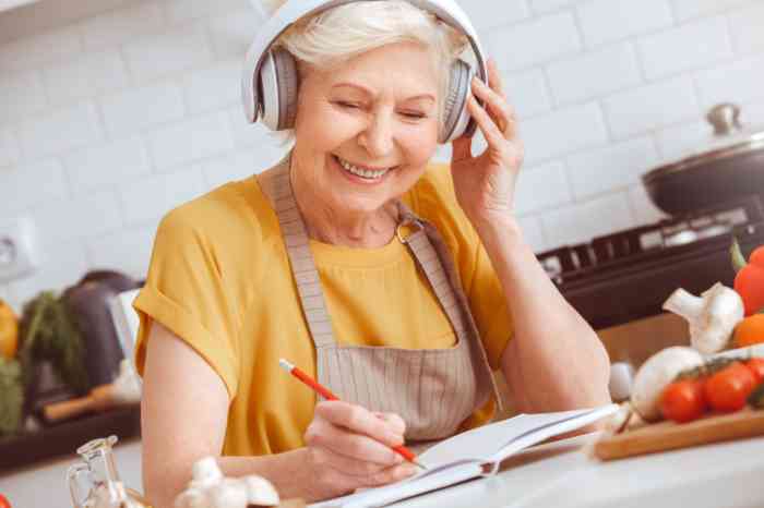 An elderly woman wearing headphones and writing in a notebook