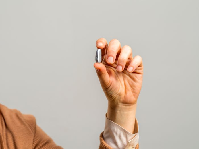 Senior woman holding a mini hearing aid 